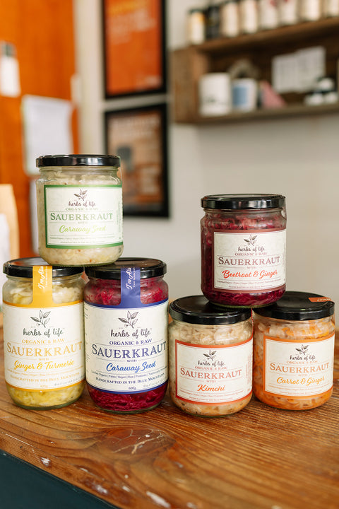 Various jars of Herbs of Life Sauerkraut on a wooden surface with a blurred background